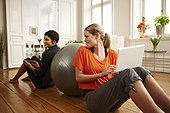 Two women sitting on floor leaning on fitness ball