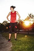 Woman in workout clothes standing near running trail at sunset