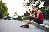 Woman in workout clothes talking on mobile phone while sitting on curb