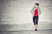 Woman in workout clothes leaning against a cement wall