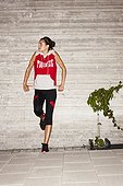 Woman in workout clothes leaning against a cement wall