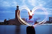 Person drawing light heart shape in air, Stockholm City Hall in background, Sweden
