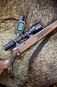 Hunting riffle with sighting telescope and walkie-talkie with wild boar in background