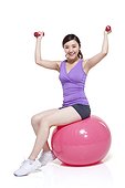 Young woman sitting on a fitness ball with dumbbells