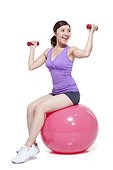 Young woman sitting on a fitness ball with dumbbells