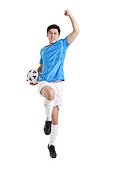 Soccer player holding a ball and jumping in celebration with arm raised into a balled fist