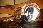 young couple in tent, man helping woman, on winter holiday in switzerland,
