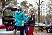Happy female joggers communicating by car in forest