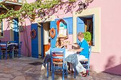 Couple eating out and drinking white wine in a small greek village in summer. Kefalonia, Greek Islands, Greece