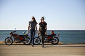 Two young women with motorcycles on empty road