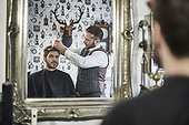 Mirror reflection of young bearded male having his hair styled in retro barber shop.
