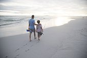 Father and son walking together along a beach with a fishing rod and tackle