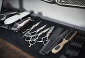 Arrangement of hairdressing scissors, brushes, combs and clippers lined up on worktop in Barber shop