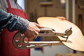 Midsection of male worker using tool to make guitar at workshop