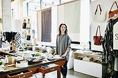 Smiling female business owner standing in boutique near table of merchandise