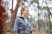 Happy fit woman holding mobile phone while looking away in forest