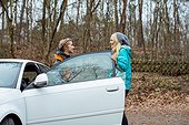 Side view of female joggers communicating at car door in forest