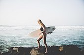 Female surfer walks along shore with board