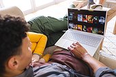 Diverse couple lying on couch and using laptop in living room at home, copy space