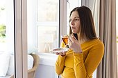 Thoughtful caucasian woman holding tea cup by window in living room at home, copy space
