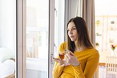 Thoughtful caucasian woman holding tea cup by window in living room at home, copy space