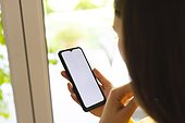 Caucasian woman using standing by window and using smartphone at home, copy space