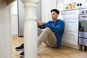 Concerned biracial man sitting on floor and holding tea cup in kitchen at home, copy space