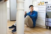 Concerned biracial man sitting on floor and holding tea cup in kitchen at home, copy space