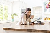 Focused caucasian woman holding mug and using smartphone in kitchen at home, copy space