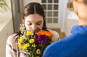 Happy diverse couple holding flowers and smelling them in kitchen at home, copy space
