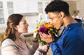 Happy diverse couple holding flowers in kitchen at home, copy space