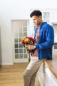 Happy biracial man holding flowers in kitchen at home, copy space