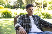 Portrait of focused biracial man sitting in chair in sunny garden, copy space