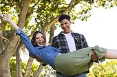 Happy diverse man holding woman in arms in air in sunny garden, copy space