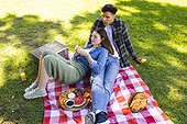 Happy diverse couple sitting on blanket and having picnic in sunny garden, copy space