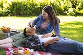 Happy diverse couple lying on blanket and having picnic in sunny garden, copy space