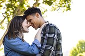 Happy diverse couple embracing and touching foreheads in sunny garden, copy space