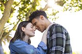 Happy diverse couple embracing and touching foreheads in sunny garden, copy space