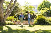 Happy diverse couple walking, holding hands and holding picnic basket in sunny garden, copy space