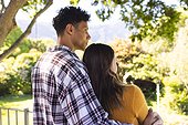 Diverse couple embracing and looking side in sunny garden, copy space