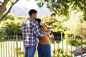 Happy diverse couple embracing and looking side in sunny garden, copy space
