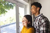 Happy diverse couple embracing and looking through window at home, copy space