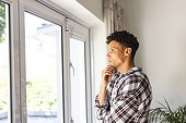Portrait of focused biracial man looking through window, holding chin with hand at home, copy space