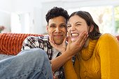 Portrait of happy diverse couple sitting on couch and making funny faces at home, copy space