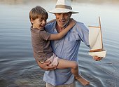 Smiling grandfather and grandson with toy sailboat wading in lake