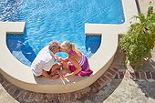 Affectionate senior couple kissing at sunny summer swimming pool