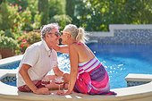Happy, affectionate senior couple kissing and drinking at swimming pool