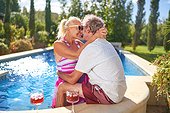 Happy senior couple hugging and kissing at sunny swimming pool
