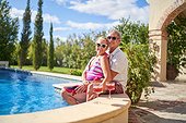 Portrait happy senior couple relaxing at sunny summer swimming pool