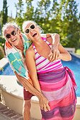 Portrait happy, playful senior couple hugging at sunny poolside